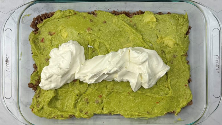 Sour cream on top of guacamole in large dish