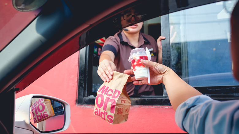 McDonald's employee hands food to a drive-thru customer