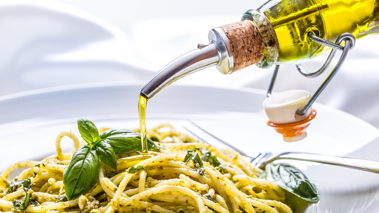 Olive oil drizzled from bottle onto pesto pasta
