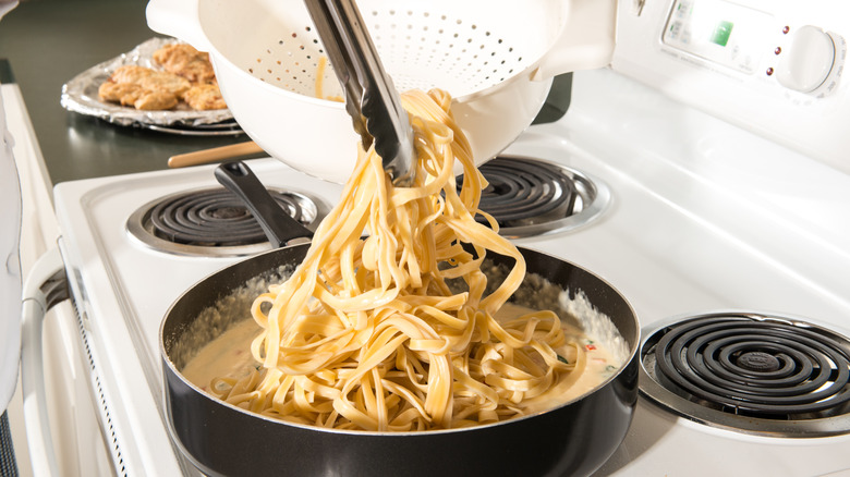 adding pasta to sauce in pan