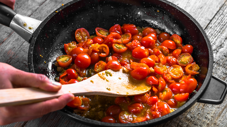 Hand stirring tomatoes in skillet