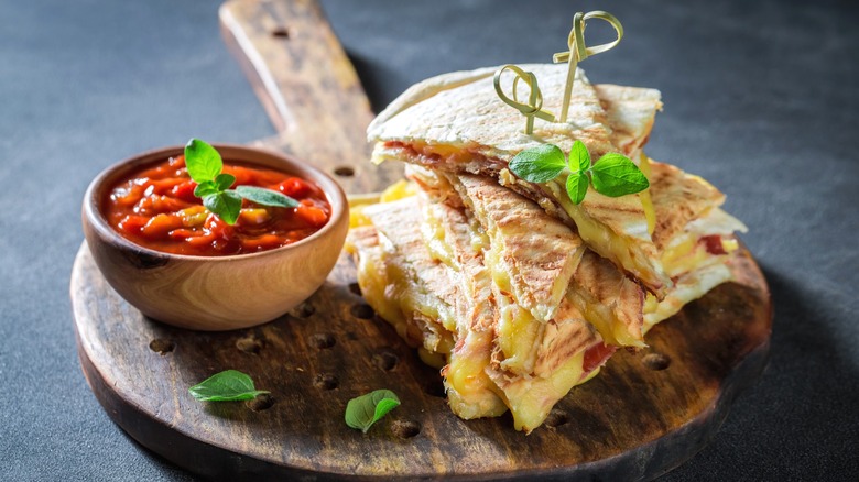 Cheese quesadilla made with ham topped with basil leaves and served with marinara sauce
