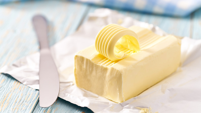 block of butter with butter knife on blue table