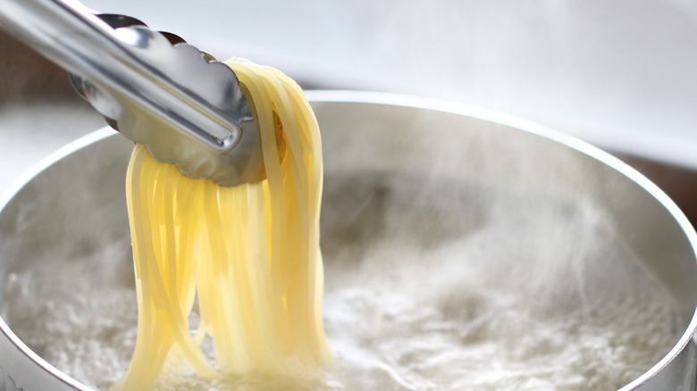 Using set of tongs to remove pasta from pan of water