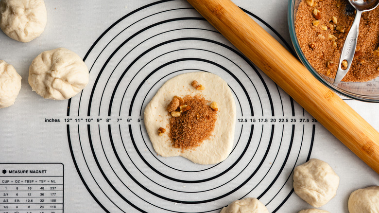 Balls of dough on measuring template with filing of nuts and brown sugar to be flattened with rolling pin for Korean hotteok pancakes.