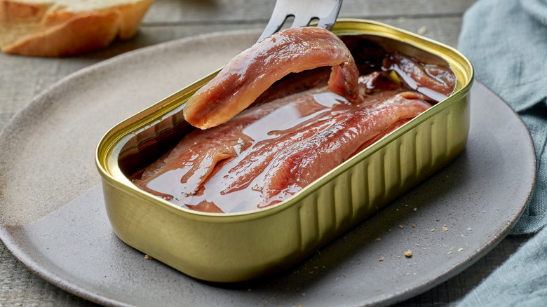 Open can of anchovies in oil with fork