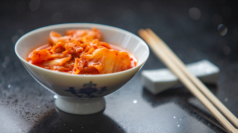 A porcelain bowl with kimchi next to chopsticks