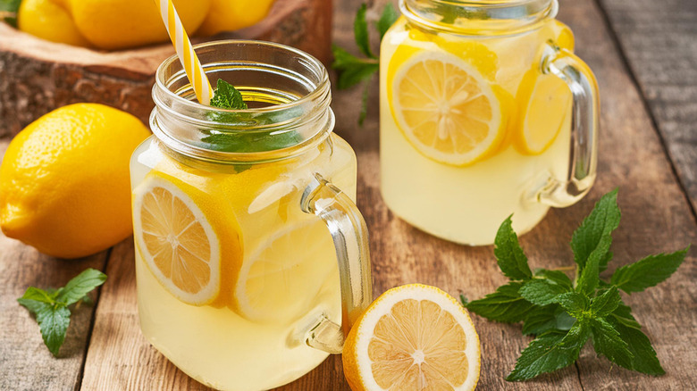 Mason jars with lemonade, lemons, mint leaves, and white and yellow straws