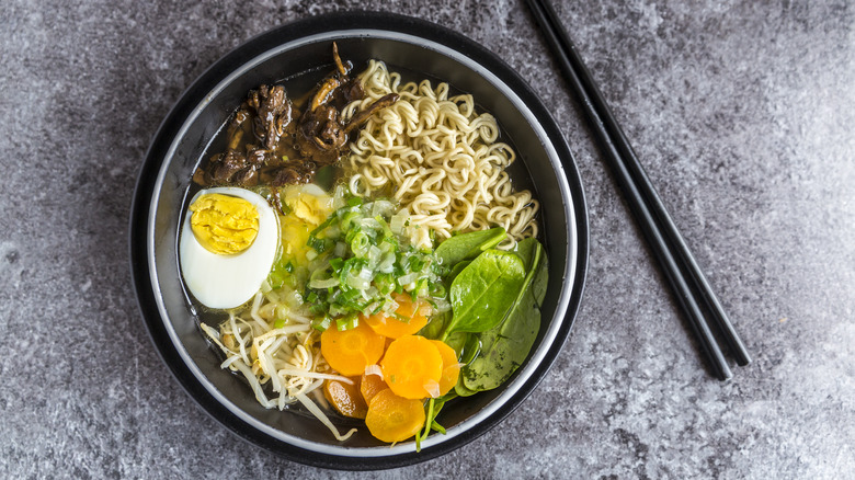 Black bowl of ramen topped with eggs, mushrooms, and vegetables