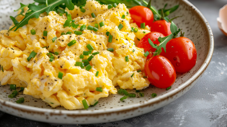 Fluffy scrambled eggs on a plate with fresh tomatoes and rocket