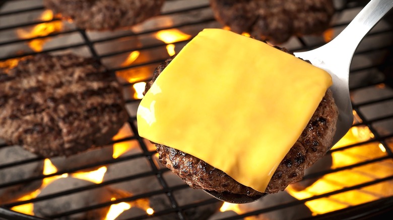 Cheeseburger patty on a metal spatula over a hot grill