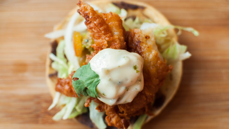 Fish sandwich topped with a creamy sauce and salad