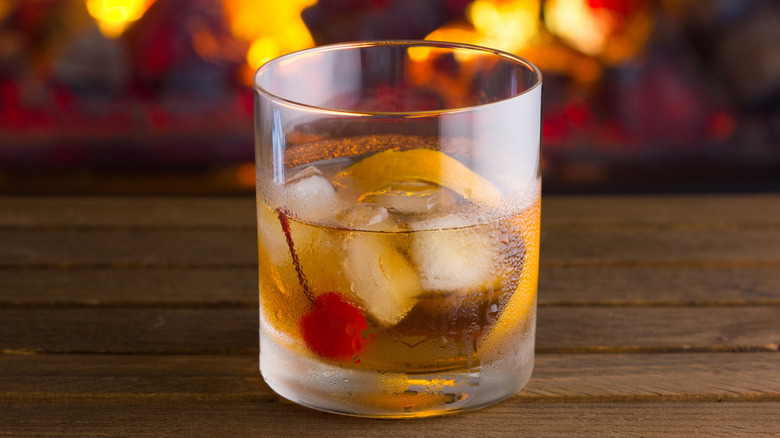 Golden color cocktail in a rocks glass with ice cubes, red cherry and orange slice