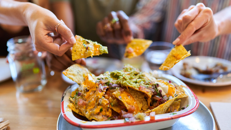 Hands reach out to grab chips from a nacho plate