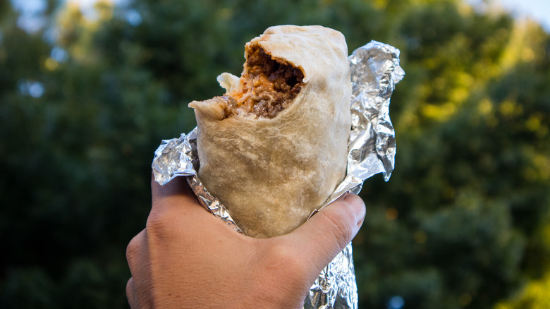 Hand holding burrito wrapped in foil