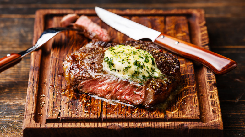 Juicy steak meat with herbed butter on wood cutting board with knife