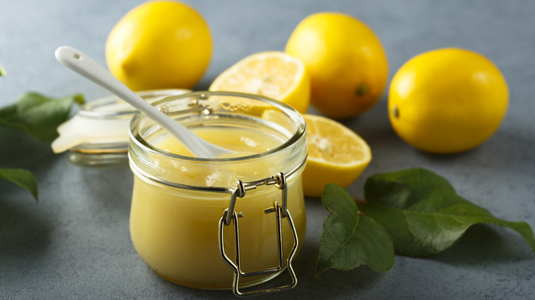 homemade lemon curd in a jar surrounded by lemons