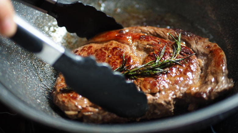 Seared ribeye steak turned with tongs in a hot pan