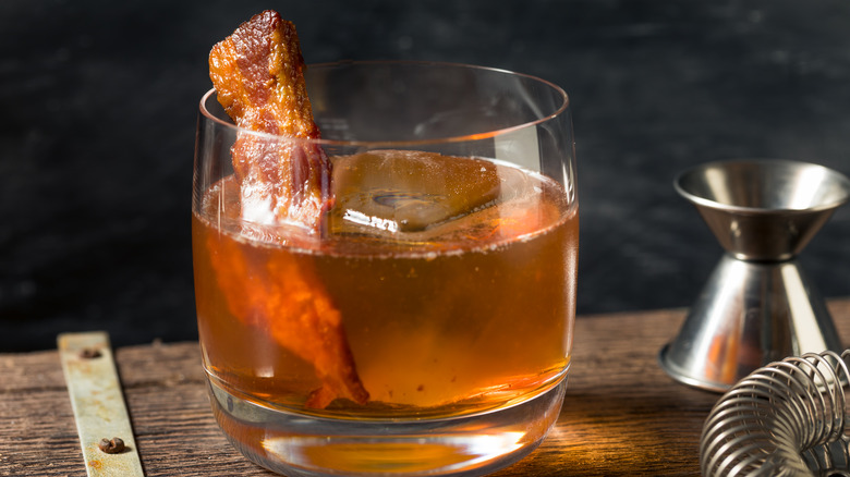 maple bacon old fashioned cocktail on a wooden table with bartending tools