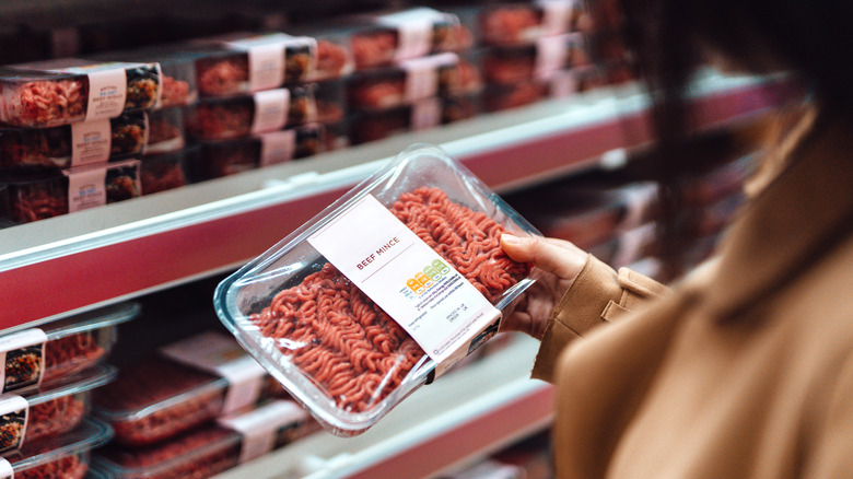 A woman holds a container of ground beef and reads the packaging