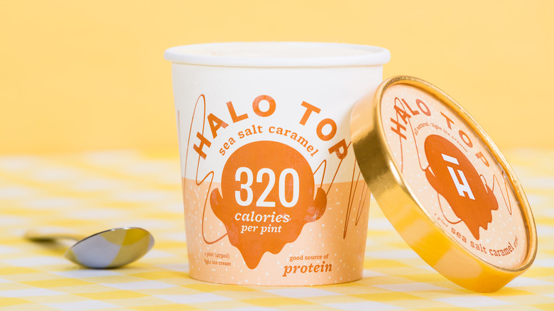 A pint of Halo Top sea salt caramel ice cream with the lid off on a yellow background