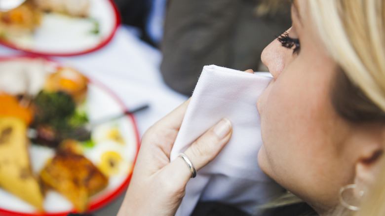 A woman wipes her face with a cloth napkin while at a fine dining restaurant