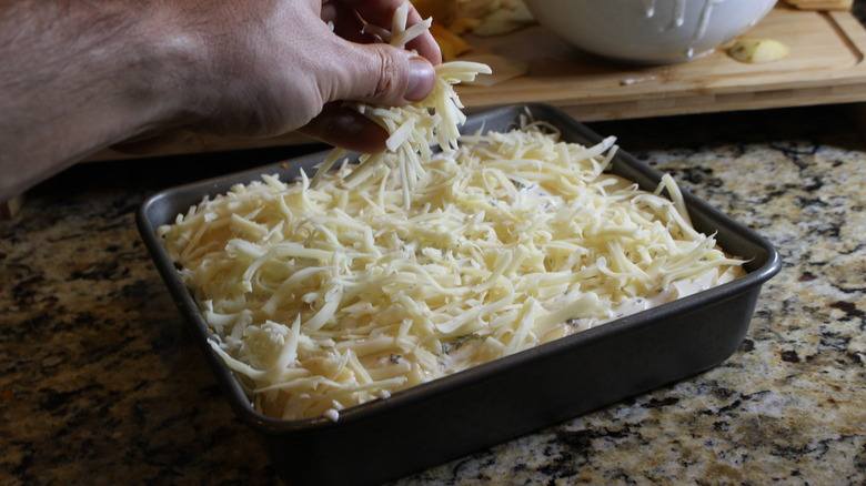 hand adding grated cheese to baking dish