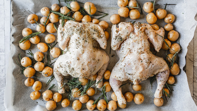 Two Cornish hens with potatoes and herbs on baking sheet.