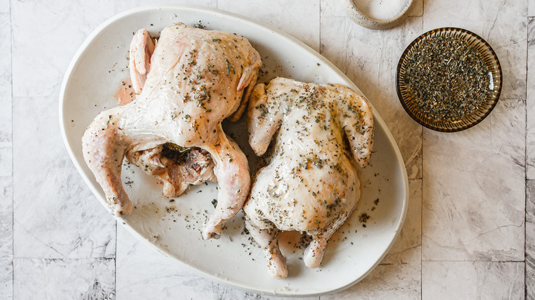 Two Cornish hens with oil and herbs on white plate.