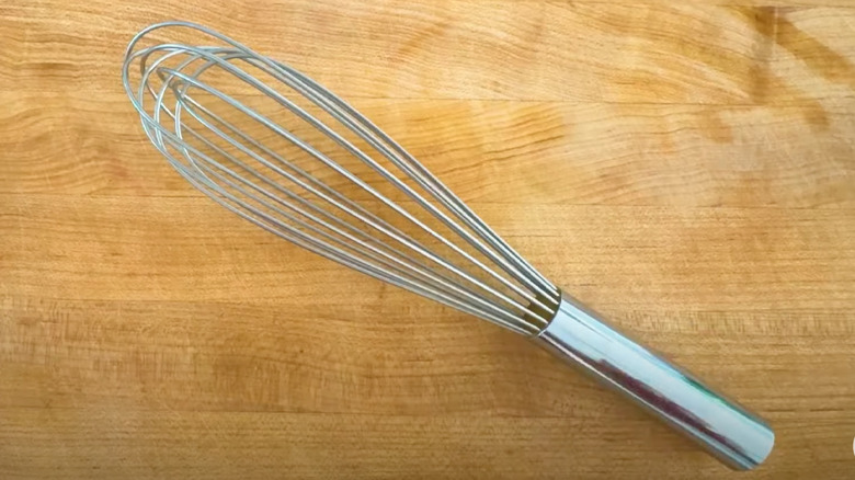 Close-up of French whisk against wooden cutting board