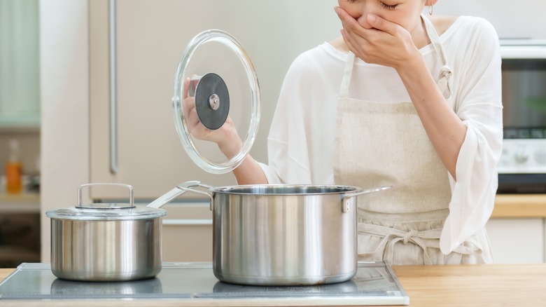 A woman clamps her hand over her mouth as she lifts the lid on a pot of smelly food