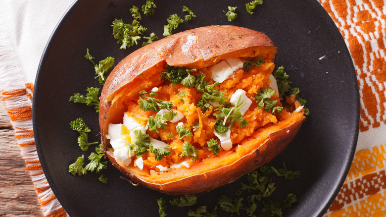 Cooked whole sweet potato topped with cheese and parsley