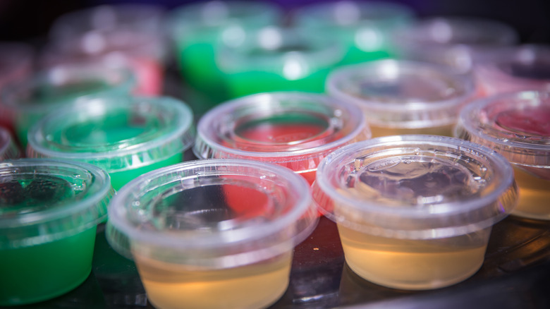 Red, green, and champagne-colored Jell-O shots sit on a black tray