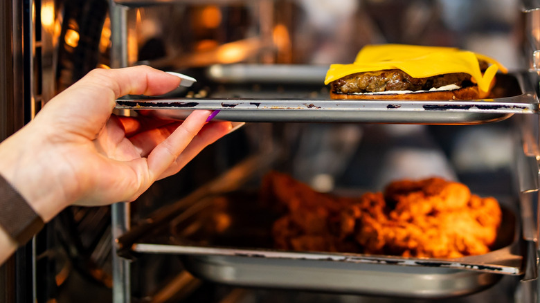 A cheeseburger being baked in the oven along with a piece of fried chicken