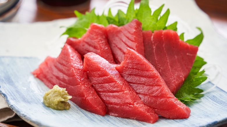 Slices of raw bluefin tuna sit on a light blue plate next to a dollop of wasabi