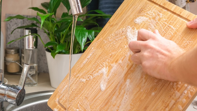 Man washing wooden cutting board in sink