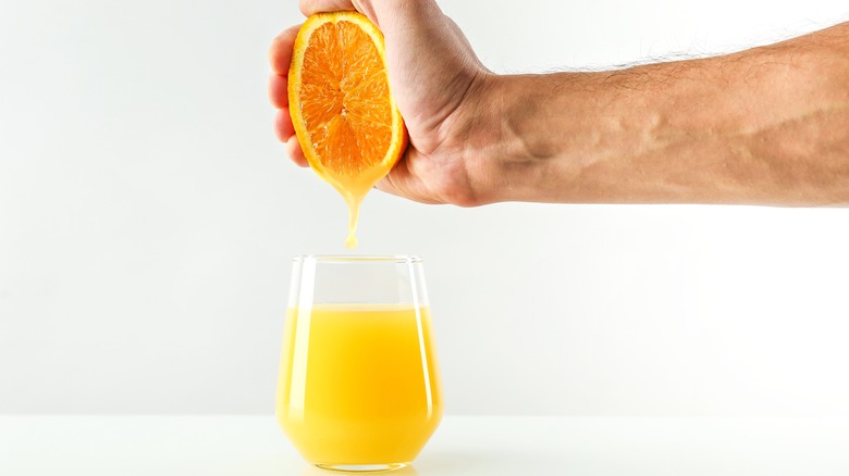 man juicing half an orange into glass