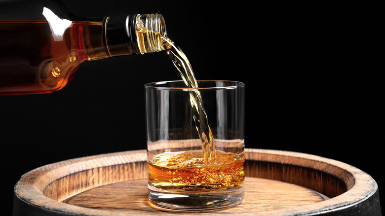 Bourbon being poured from glass bottle into a rocks glass on a wooden tray