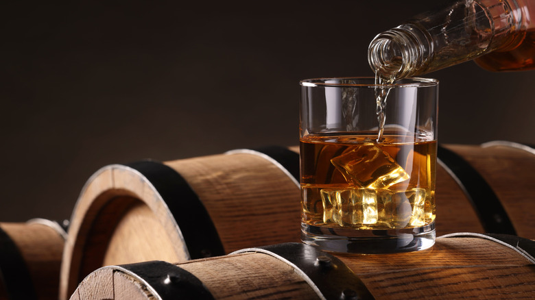 Pouring bourbon into a glass on a barrel