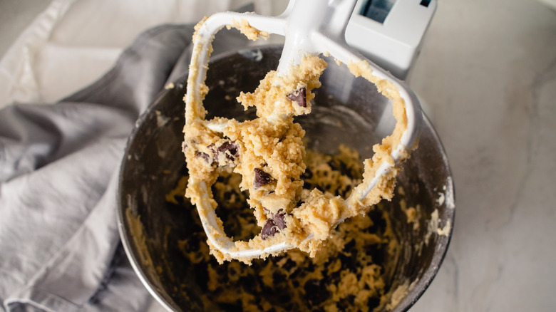 Mixing tool attached to a stand mixer covered in chocolate chip cookie dough