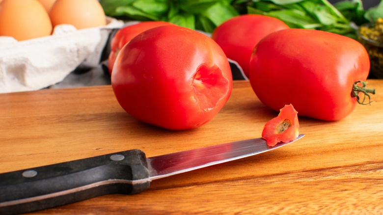 Plum tomatoes and a knife laying on a wooden cutting board.