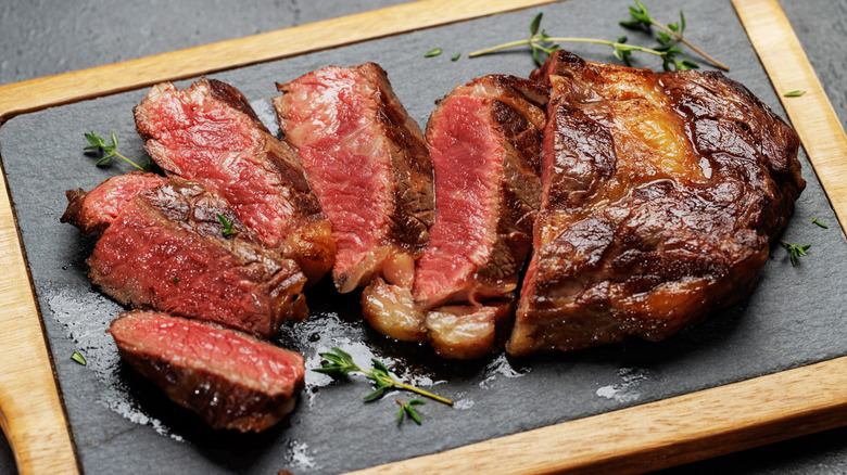 Sliced cooked ribeye on a board with sprigs of thyme