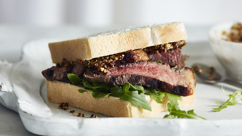 A ribeye steak sandwich with greens and mustard