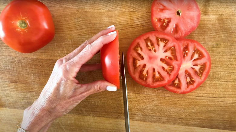 Serrated knife cutting through whole tomato