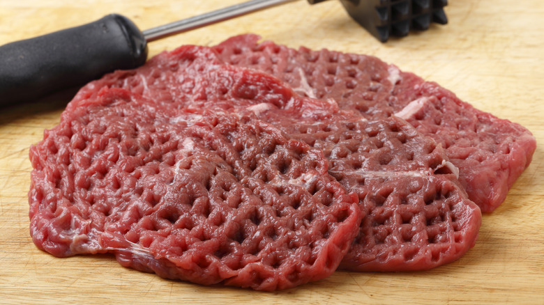 Three raw cube steaks on wooden board