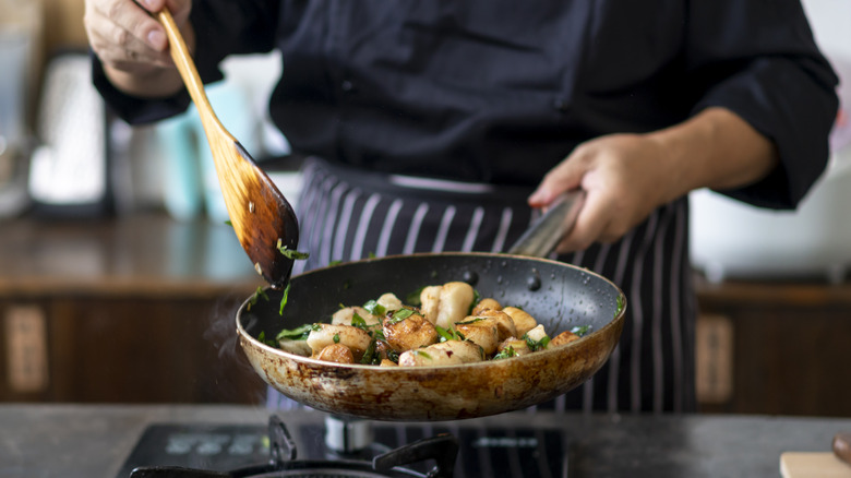 Cook stirring a pan  of shrimp with wooden spoon over a single burner