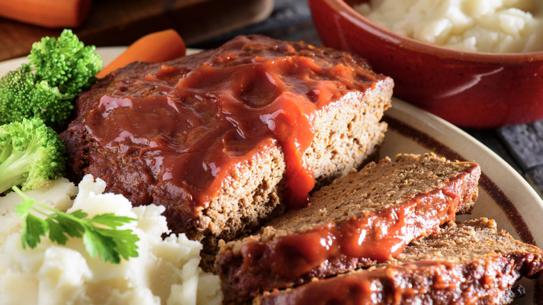 Sliced meatloaf on a plate with vegetables and mashed potatoes