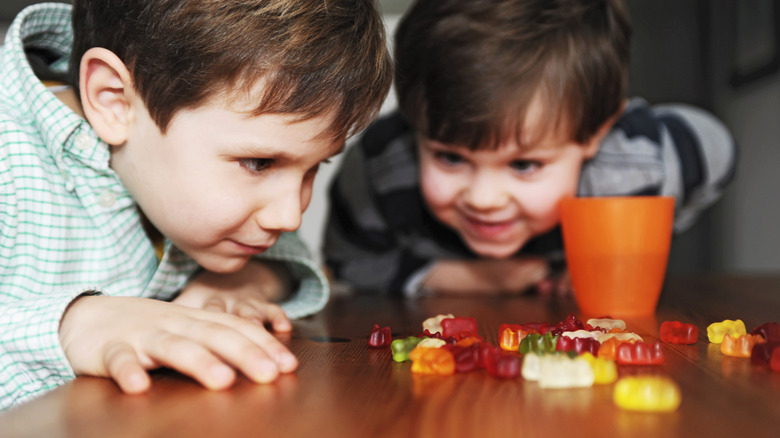 Two young boys looking closely at their gummy candies scattered on a wooden table