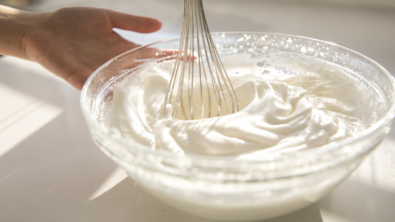 Person stirring large mound of whipped cream in a glass bowl