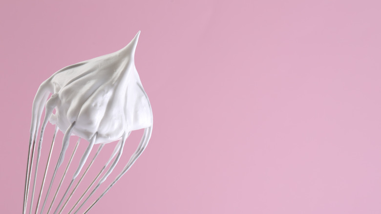 Whisk with folds of cream, sitting on a pink background